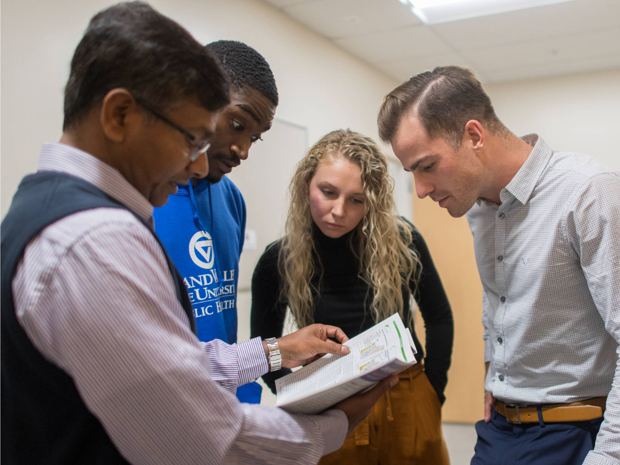 Three students peer intently into a reference book being used by the faculty instructor